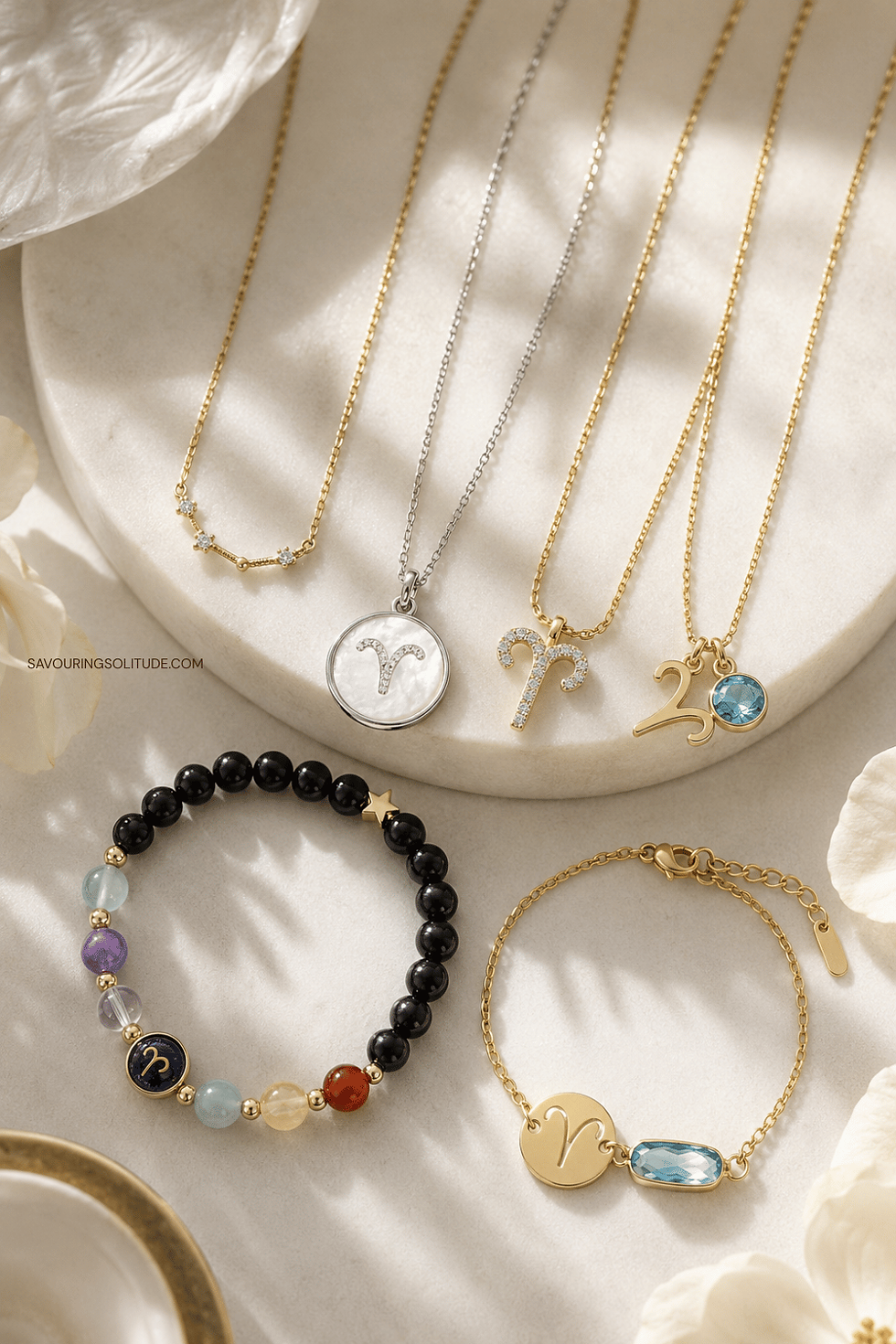 Aries zodiac jewelry flat lay featuring gold and silver necklaces with Aries ram symbol pendants, mother-of-pearl medallion, black onyx gemstone bracelet, and blue topaz charm bracelet