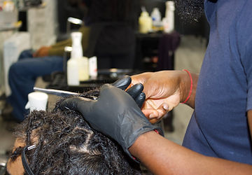 Staff at Q2 Locs Parlour trimming the body of a client's locs.