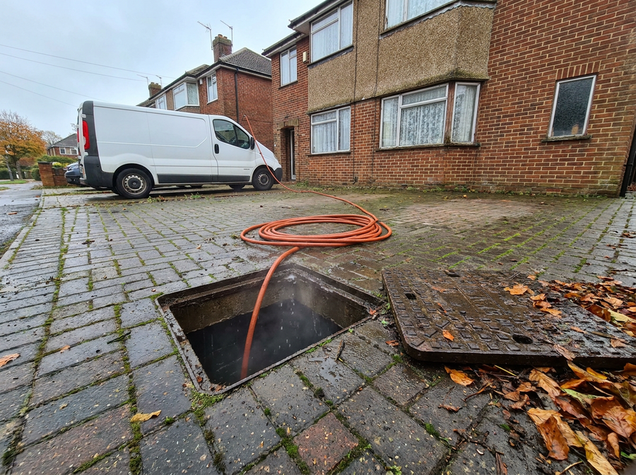 Open drain inspection chamber with a high-pressure jetting hose on a block-paved driveway in Poole, Dorset