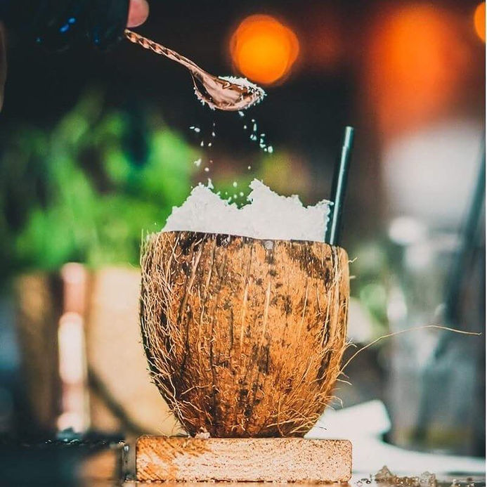 קוקטייל טרופי מרענן בקליפת קוקוס, יד מפזרת סוכר מעל.