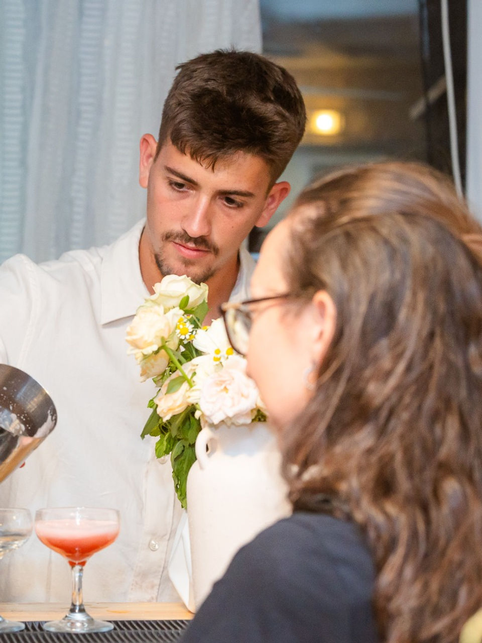 ברמן צעיר מוזג קוקטייל אדום משייקר לשני אורחים בבר.