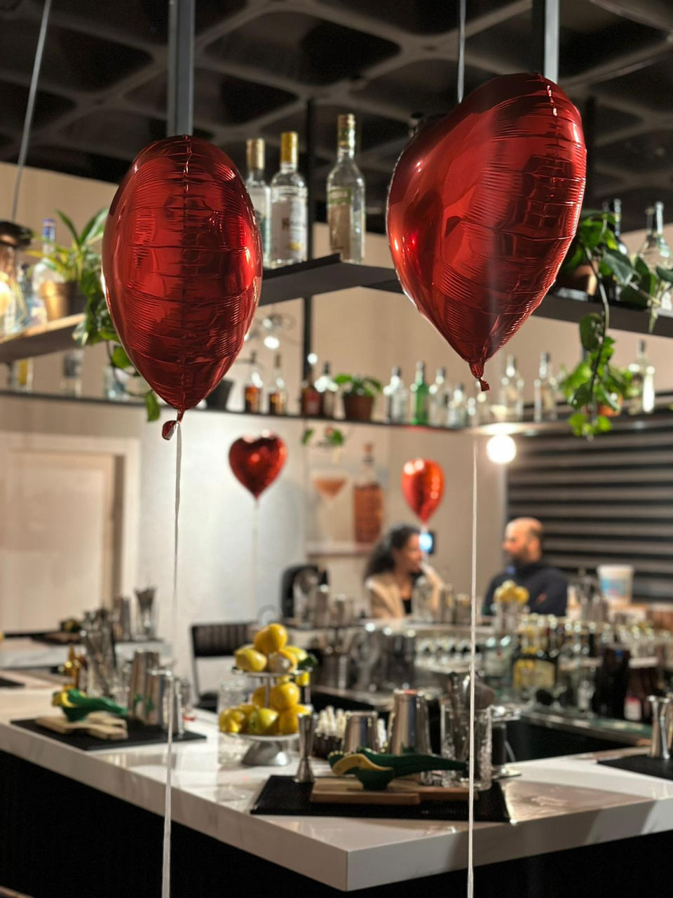 בלונים אדומים בצורת לב תלויים בבר עם בקבוקים ולימונים על הדלפק.