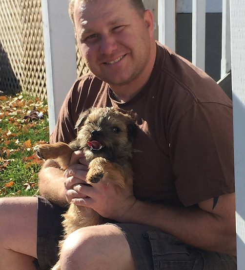 smiling man holding dog, border terrier,