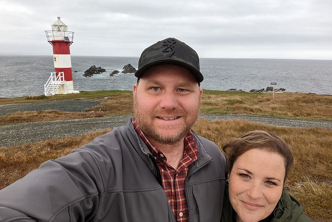 Two people standing in front of a lighthouse and ocean