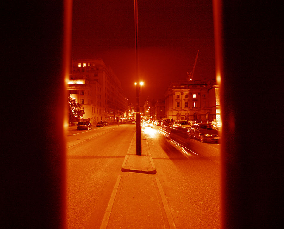 An orange hued view along a street at night, seen between two columns