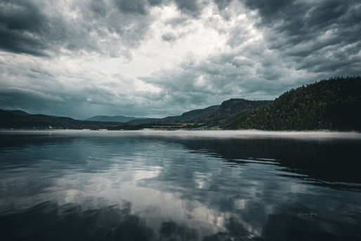 Vue sur l'Anse-Saint-Jean, Saguenay, Qc. Plan d'eau tranquille miroitant les nuages et la brume de début de soirée.