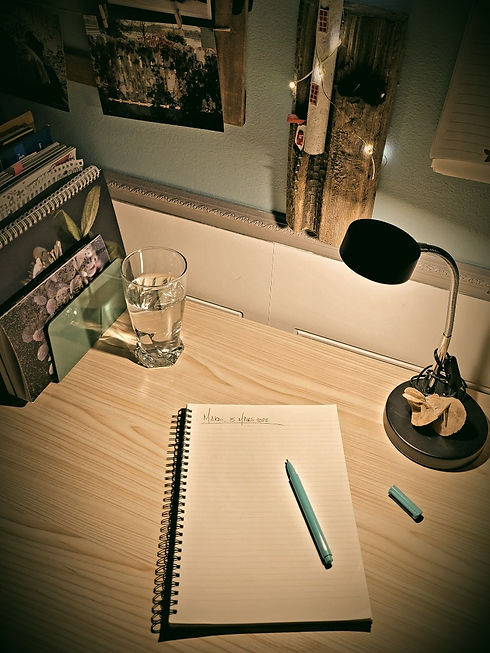 Mon bureau de travail sur lequel est déposé un cahier de notes et un stylo, le tout éclairé par ma lampe de bureau