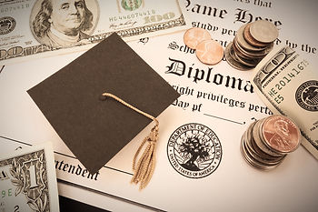 a college graduation cap sitting on a diploma, with dollar bills and change around it.