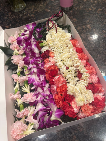 Graduation orchid lei, tuberose and pink carnation lei, red and orange spiral lei with ti leaf rope, and a white pikake lei.