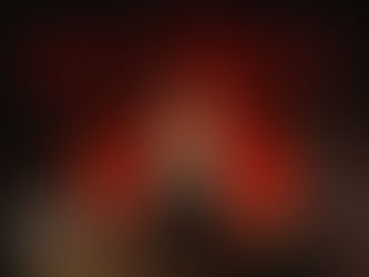 An older man with gray dreadlocks and a long beard stands at an altar with eerie red lighting