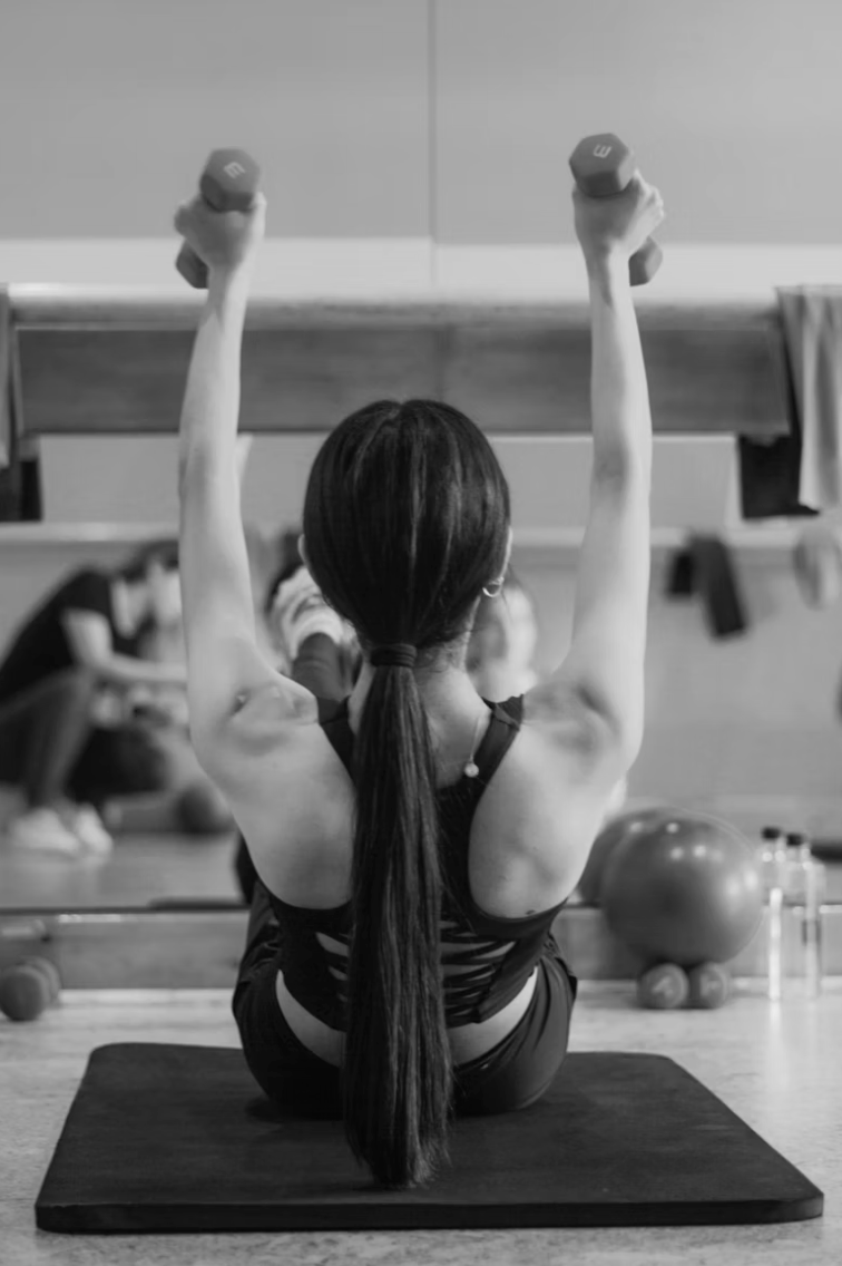 Close-up view of a Pilates instructor demonstrating a beginner exercise with a single student in a bright studio
