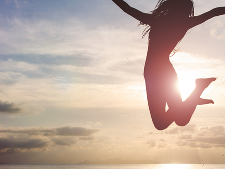 Woman jumping in the air at the beach during sunrise, symbolising freedom and a fresh start.
