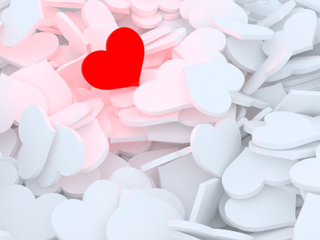 A single bright red heart stands out among dozens of soft white and pale pink heart shapes scattered across the image. The red heart is positioned near the centre and draws immediate attention, symbolising individuality, self-love, resilience, or standing apart from the crowd. The overall design has a clean, minimalist aesthetic with soft lighting and gentle shadows.