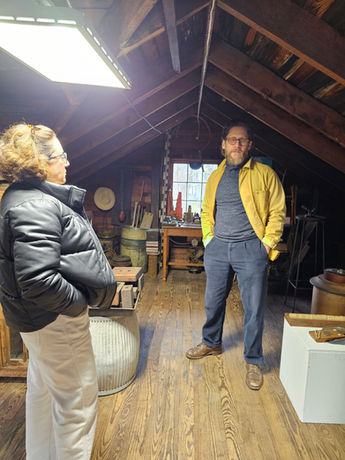 Two people in an attic with old wooden objects and a window.