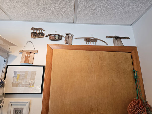 Rustic wooden art pieces displayed on a white wall above a wooden cabinet.