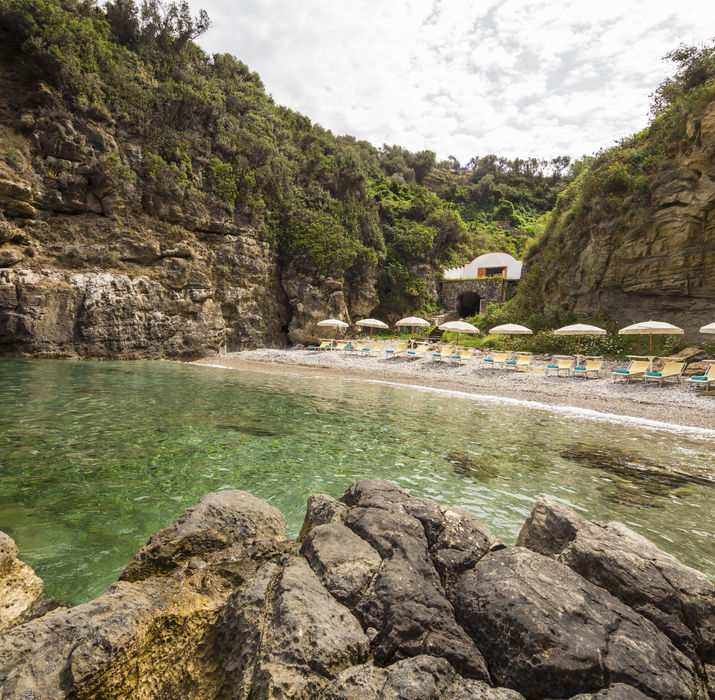 Secluded Mediterranean cove beach with rocky outcrops and lush hills, ideal for swimming or a beach excursion near the retreat.