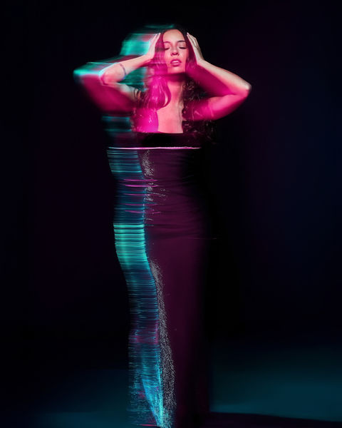 A woman in a black dress surrounded by teal and magenta light trails using long exposure and slow shutter motion blur.