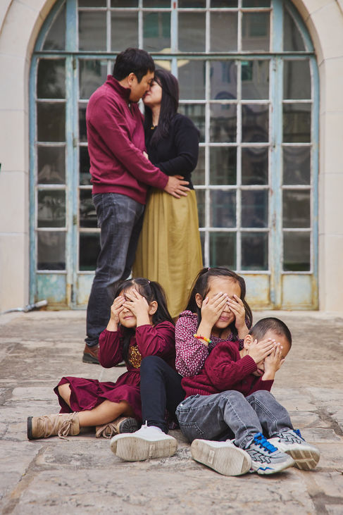 Parents sharing a moment while their three children cover their eyes during a playful family session at UT Austin.
