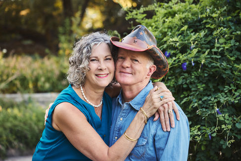 Couple smiling and embracing closely during their Georgetown TX anniversary photoshoot in a garden full of green plants and morning light.