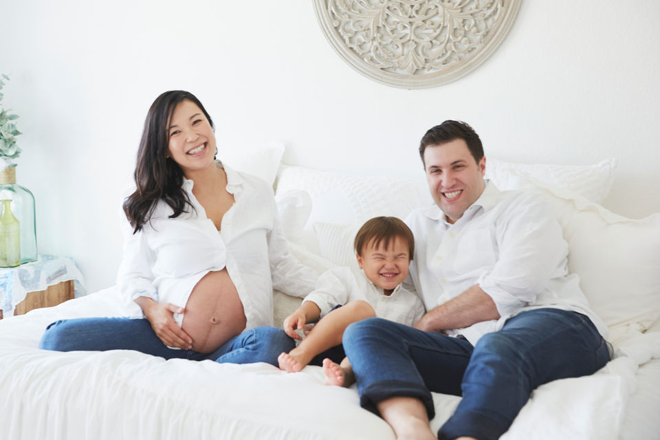 Bright lifestyle maternity photography of a family relaxing together on a bed