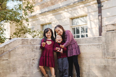 Three siblings smiling and standing together on stone steps at UT Austin.