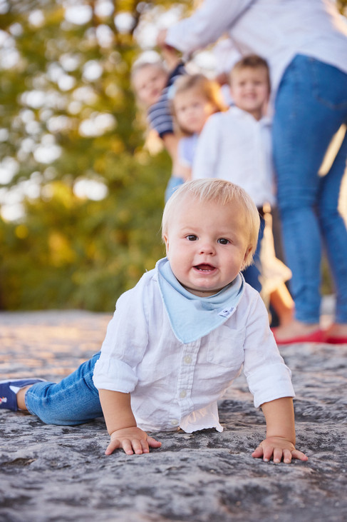 Close-up of baby with blurred family in the background — captured in warm sunset light at McKinney Falls State Park, Austin.