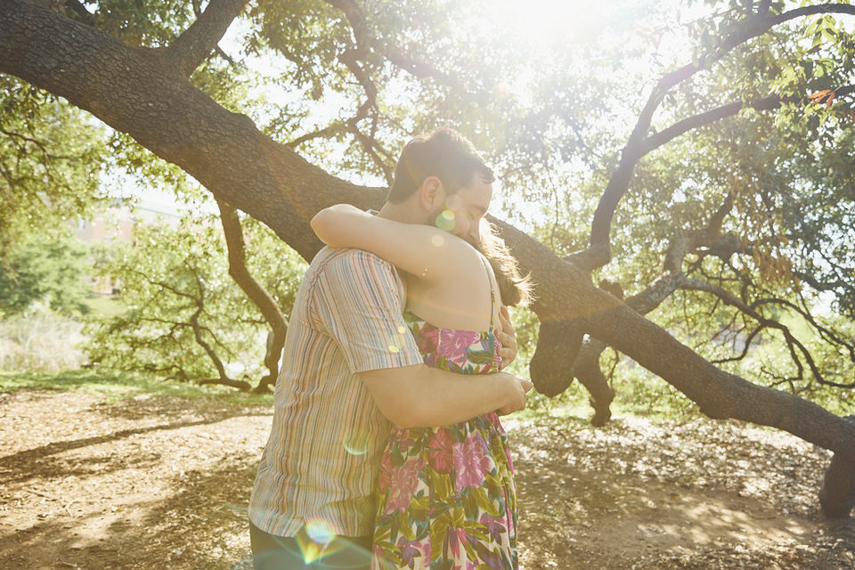 Couple hugging under oak trees with warm sunlight during an Austin couples session