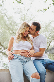 Husband kissing his pregnant wife on the forehead under the trees during a serene morning maternity session in Austin.