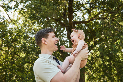 Bull Creek District Park family photos of a father lifting and smiling at his baby daughter outdoors in Austin