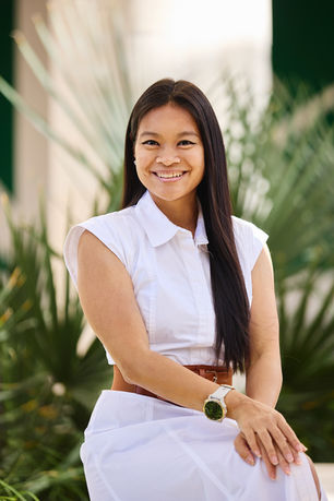 Business portrait of a woman sitting and smiling, wearing a white dress with a brown belt, photographed at Blanton Museum of Art in Austin with modern green architectural background.