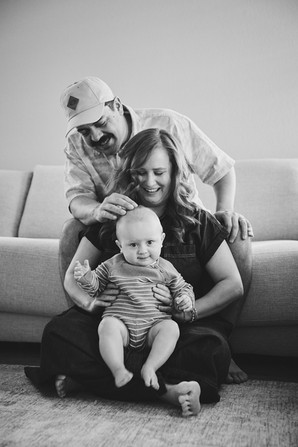 A family of three, parents and a baby boy laughing on the sofa
