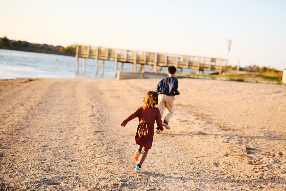 Children running along the sandy shore at Lake Pflugerville Park, candid family photo session