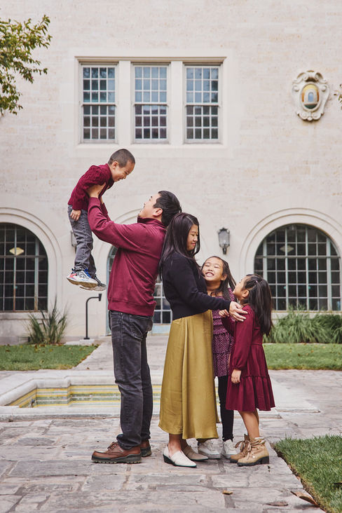 Father lifting his young son as the rest of the family smiles at UT Austin during their photo session.