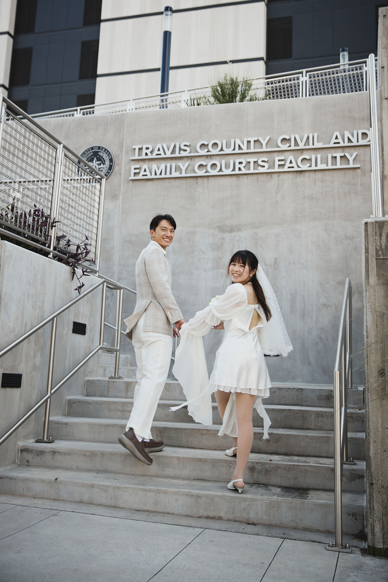 Bride and groom walking up the steps of the Travis County Courthouse in downtown Austin, holding hands and smiling