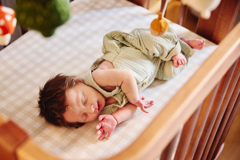 Newborn baby sleeping on their side in a wooden crib, wearing a soft green outfit, photographed during an in-home newborn session.