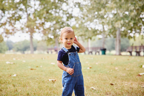 Toddler wearing overalls standing on the grass at Mueller Lake Park during a fall family session.