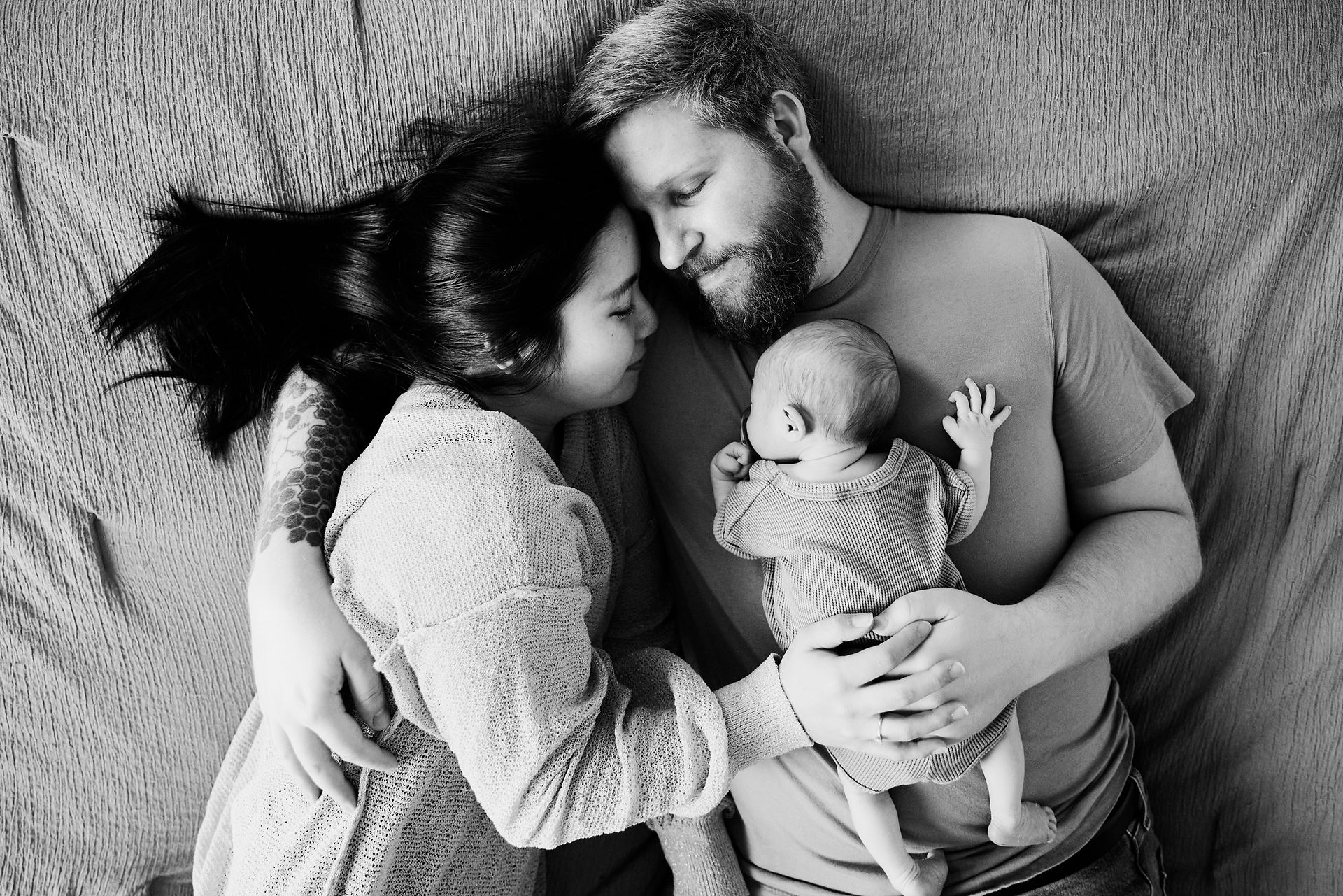 In-home newborn photography in Austin showing parents resting with their newborn on a bed