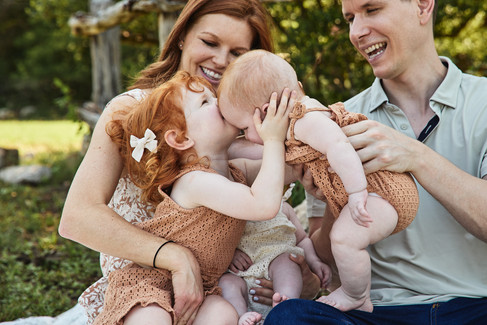 Bull Creek District Park family photos capturing a sweet sibling moment between a young girl and one of the twin baby sisters