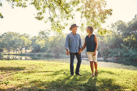 A couple walking hand in hand by the San Gabriel River in Georgetown TX during their 45th wedding anniversary morning photoshoot, surrounded by golden sunlight and peaceful nature.