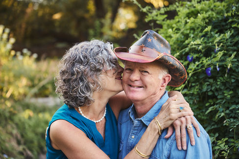 Woman kissing her husband on the cheek during their 45th wedding anniversary photoshoot at Sunken Garden Georgetown TX, surrounded by lush greenery.
