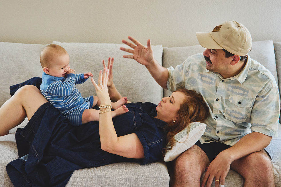A family of three, parents and a baby boy laughing on the sofa