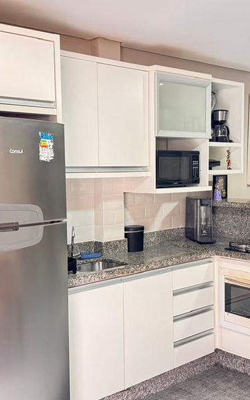Cozinha planejada branca com geladeira inox e churrasqueira.