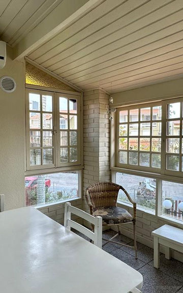 Varanda envidraçada do Apartamento 34 com mesa branca e cadeiras de vime.