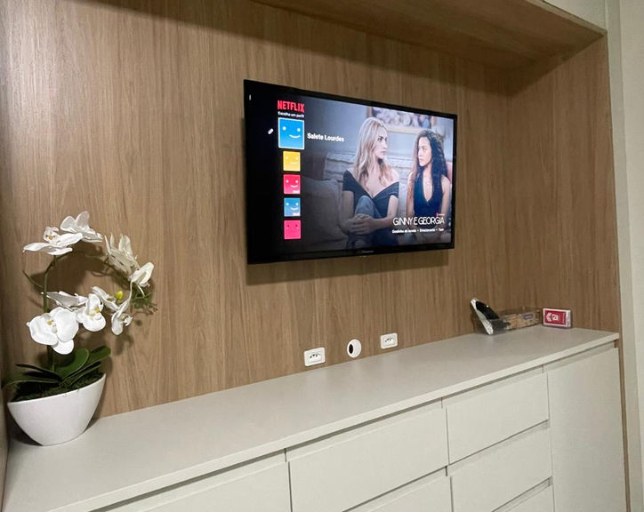 Painel de TV em madeira com aparador branco e orquídeas.