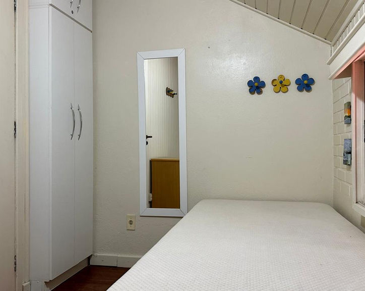 Quarto compacto com cama, armário branco e espelho vertical.