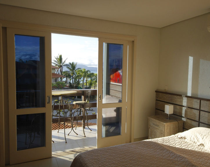 Quarto com cama de casal e varanda com vista para palmeiras.