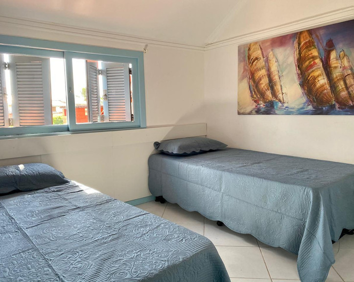 Quarto com duas camas de solteiro e quadro de barcos.