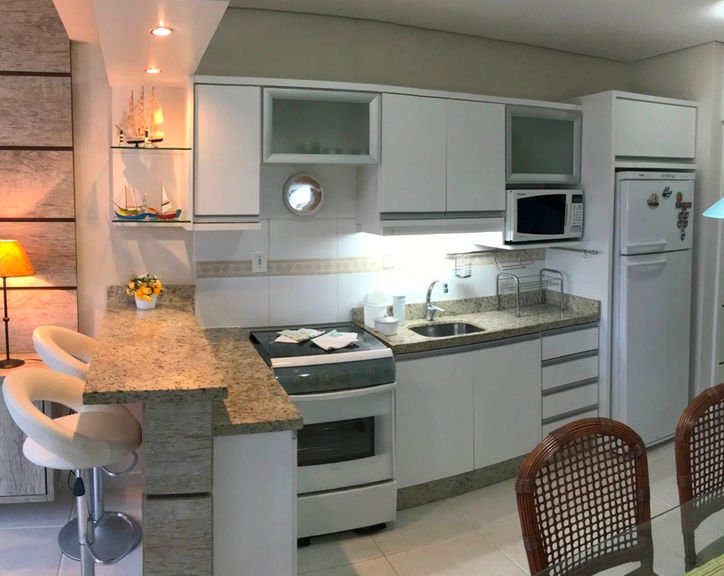 Cozinha planejada branca com bancada de granito e banquetas.