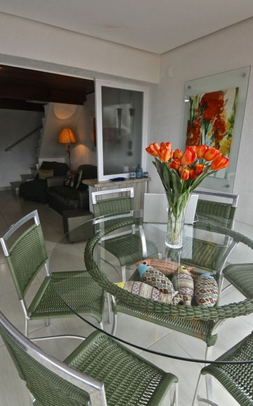 Varanda do Apartamento 29 com mesa de vidro e cadeiras verdes