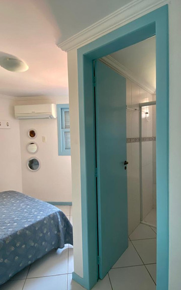 Quarto com cama de casal e porta azul aberta para o banheiro.